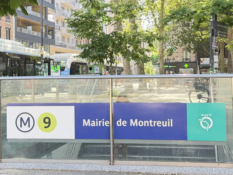 Bouche du métro Mairie de Montreuil, ligne 9, sur une place plantée d’arbres, des bus derrière.
